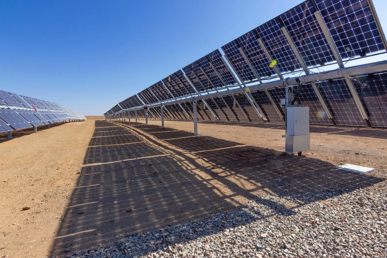 Elevated rows of ground-mounted solar panels casting shadows on gravel